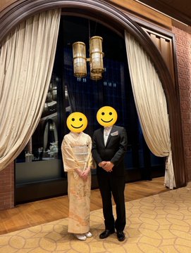 The image features a man and woman standing next to each other, both wearing traditional Japanese clothing. They are posing for a picture together, with the woman's face partially visible behind her. The background of the photo includes an archway or doorway that is decorated with two hanging lamps, adding an elegant touch to the scene.