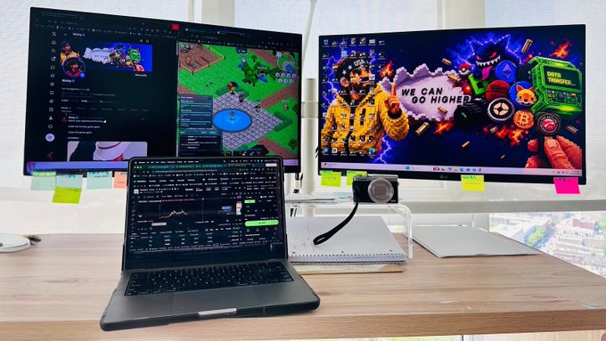 A trader works at a multi-monitor workstation displaying crypto charts and a "WE CAN GO HIGHER" Bitcoin-themed wallpaper, with a laptop running trading analytics. The setup reflects the intense focus of "locking in" for a 1-2 hour trading session on $KINS with Solana this cycle.