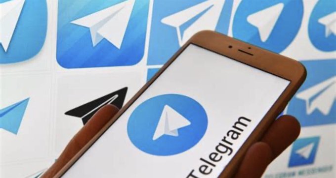 A hand holds a smartphone displaying the Telegram app logo against a backdrop of repeated Telegram paper plane icons.