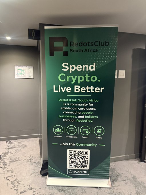 A green RedotsClub South Africa banner stands in a hallway, promoting their crypto community with the tagline "Spend Crypto. Live Better" and featuring icons for Connect, Collaborate, Spend, and Grow, alongside a QR code to scan and join the community. The banner reflects the post's theme of crypto education and Web3 engagement at DDCapeTown, highlighting RedotsClub as a potential platform for learning and building in the crypto space.