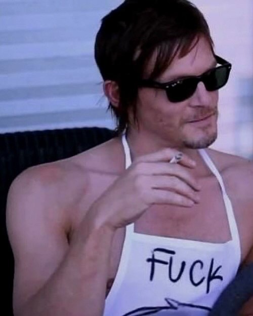 A photo of a man with sunglasses wearing a white apron with the word 'FUCK' written on it, holding a cigarette.