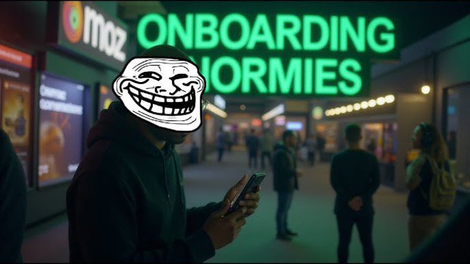 The image features a man wearing a hoodie with a face drawn over his eyes, holding a cell phone and smiling at the camera. The background includes a neon sign for "Onboarding Normies" and other people walking around. There are also two backpacks visible in the scene - one near the center of the image and another towards the right side.