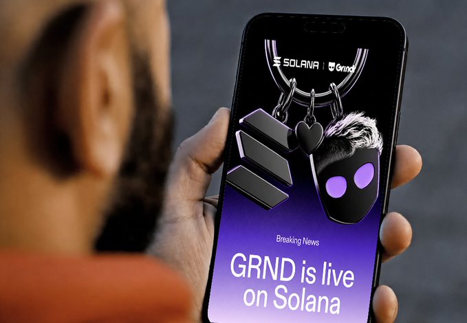A person holds a smartphone displaying a promotional announcement reading "Breaking News: GRND is live on Solana," featuring Solana and Grnd branding alongside keychain-style icons on a purple background. The image visually reinforces the post by showcasing the official launch announcement of the GRND token on the Solana blockchain.