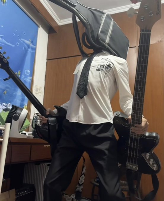 A person dressed in a white shirt, tie, and black pants holds a bass guitar in a room with wooden walls and a blue ocean-themed banner.