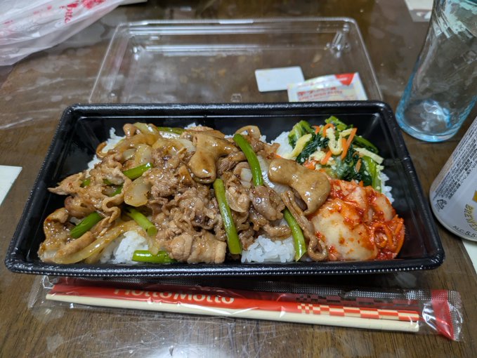 A Japanese bento box meal containing rice topped with meat and vegetables, kimchi, and greens, with Tosajiro chopsticks on the side.