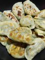 Close-up photo of a plate of pierogi or dumplings, showing several pieces with various fillings visible at the edges.