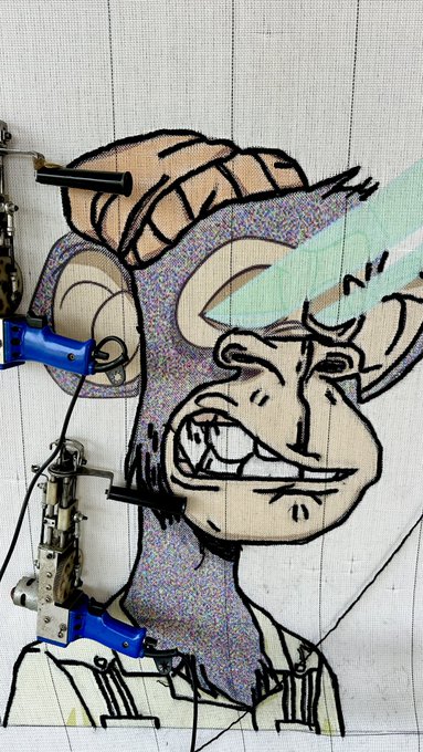 A robotic tufting machine is creating a custom rug featuring a stylized Bored Ape Yacht Club character design, with multicolored yarn being applied to the canvas. The image captures the in-progress craftsmanship of what is described as the first-ever "beam wool" rug made for a BAYC collector, showing the detailed artwork taking shape under the industrial needle tool.