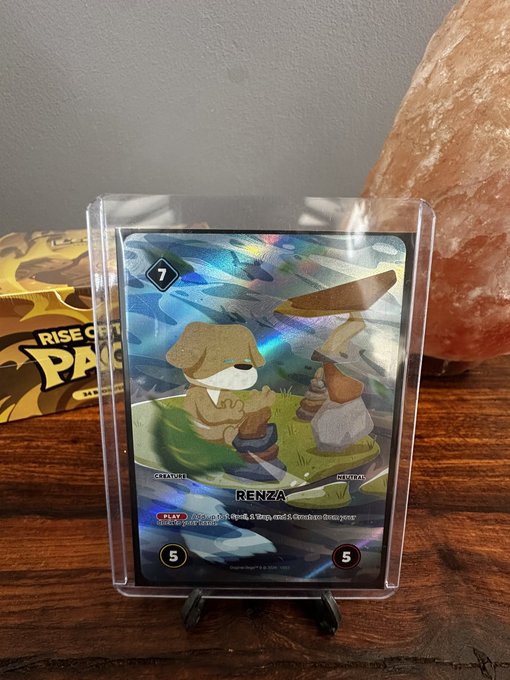 A holographic trading card featuring the character 'RENZA' (a dog creature) is displayed on a stand next to a Himalayan salt lamp.
