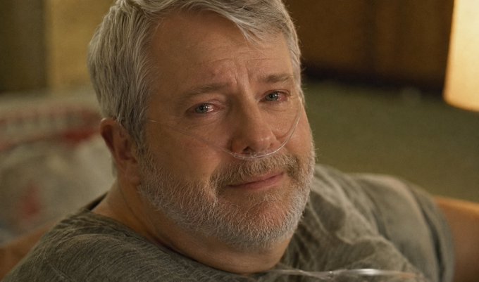 Close-up of an older man with a gray beard wearing a nasal cannula, looking softly toward the camera.