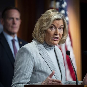 A woman in a light-colored blazer speaks at a podium during a press conference, with an American flag visible in the background and a man in a suit standing behind her. The image, paired with the post announcing the advancement of the CLARITY Act in U.S. law enforcement discussions, suggests a congressional or political announcement related to cryptocurrency regulation.