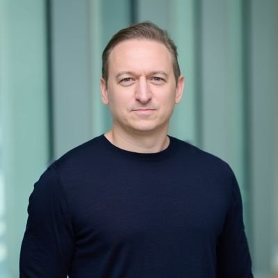 The image features a man wearing a dark blue sweater, standing against a green background with white vertical lines. The man appears to be looking directly at the camera, giving off an air of confidence or professionalism. The caption below the photo reads "@PierreSamaties shared that he's looking forward to joining the @UNDP Blockchain Advisory Group A strong signal for broader institutional engagement around blockchain and digital infrastructure Interesting to see experienced voices from the $ICP ecosystem contributing at". This suggests that the man might be involved in a project or initiative related to blockchain technology, possibly working with the United Nations Development Programme (UNDP) on issues such as digital inclusion and financial inclusion.