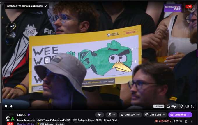 The image shows a group of people sitting together watching a video or TV show with a large sign featuring an angry bird character. The sign has the words "Wee wo" written on it. There are at least ten people visible in the scene, some sitting closer to the camera and others further away. They appear to be engaged in the content being displayed on the screen.

The post includes information about a video or TV show that has been watched by over 500K viewers. It also mentions that the game is breaking records for both teams involved. The post seems to be related to a gaming event, possibly an online streaming platform like Twitch or YouTube.