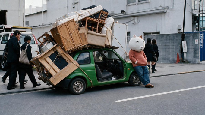 A small green car is precariously overloaded with furniture and household items stacked high above its roof, while a person in a large white cat-head mask and pink sweater stands casually beside it, embodying the meme's "go all-in, don't be cautious" energy.

The image humorously captures the meme's spirit of reckless overcommitment—just as the car is burdened far beyond its capacity, the $KET token (Kekius Maximus) encourages traders to pile in without hesitation, dismissing traditional risk management in favor of bold, high-risk positioning.