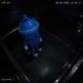 A dark, low-resolution image showing a small blue figure or object inside what appears to be a metallic box or container.