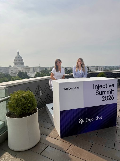 Two smiling women stand behind a "Welcome to Injective Summit 2026" podium on a rooftop terrace with the U.S. Capitol building visible in the background, tying into the post's coverage of the crypto event held on Capitol Hill.