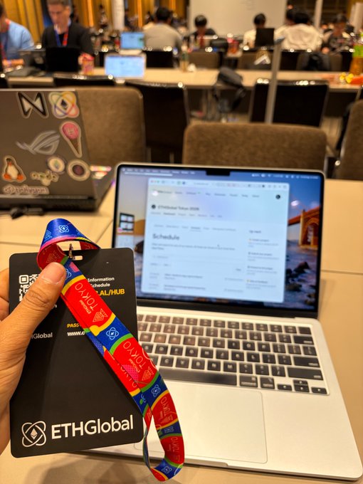 A hand holding an ETHGlobal badge and colorful lanyard in front of an open laptop displaying a webpage about a festival/hackathon schedule.