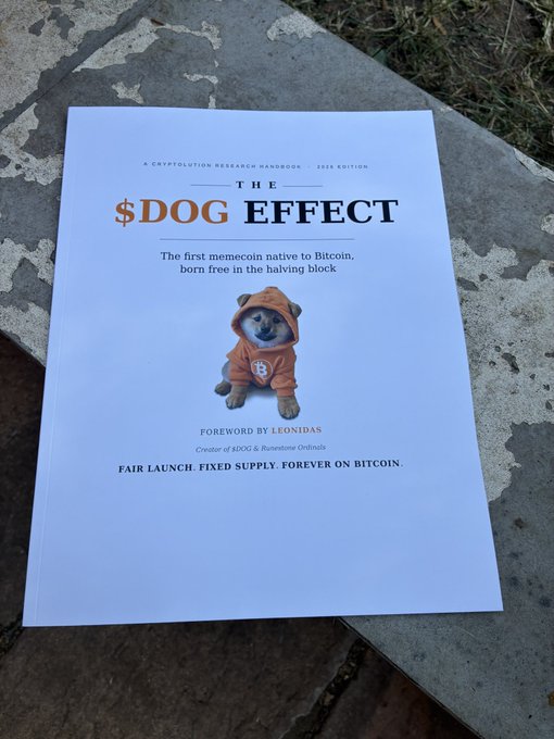 A printed book or pamphlet cover titled 'THE $DOG EFFECT' with the subtitle 'The first memecoin native to Bitcoin, born free in the halving block,' featuring an image of a Shiba Inu dog wearing an orange Bitcoin hoodie.
