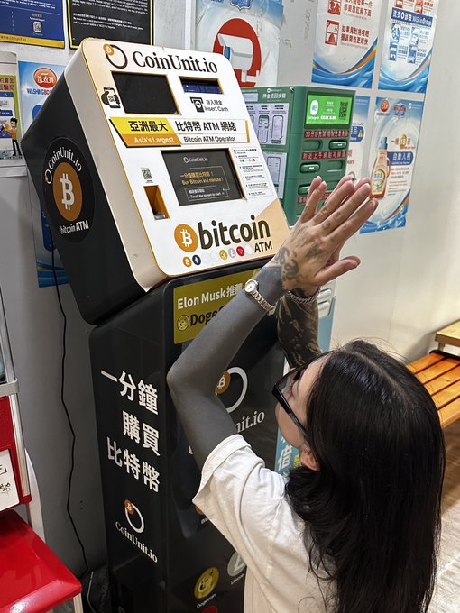 A young woman poses with raised arms in front of a CoinUnit.io Bitcoin ATM in Asia, featuring bilingual Chinese-English text advertising "Asia's Largest Bitcoin ATM Operator" and "Buy Bitcoin in 1 Minute." The image humorously reinforces the post's "fiat died for our sins" message, depicting a near-religious devotion to Bitcoin via the very machines designed to convert fiat currency into crypto.