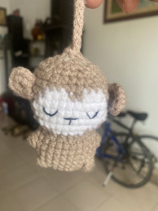 A small crocheted beige and white sheep/lamb keychain with closed eyes is held up indoors.