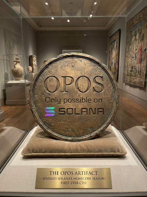 A museum-style display showing a large bronze medallion engraved with 'OPOS Only possible on SOLANA' on a cushion, with a plaque below reading 'THE OPOS ARTIFACT - SPARKED SOLANA'S MEMECOIN SEASON - FIRST EVER CTO'.
