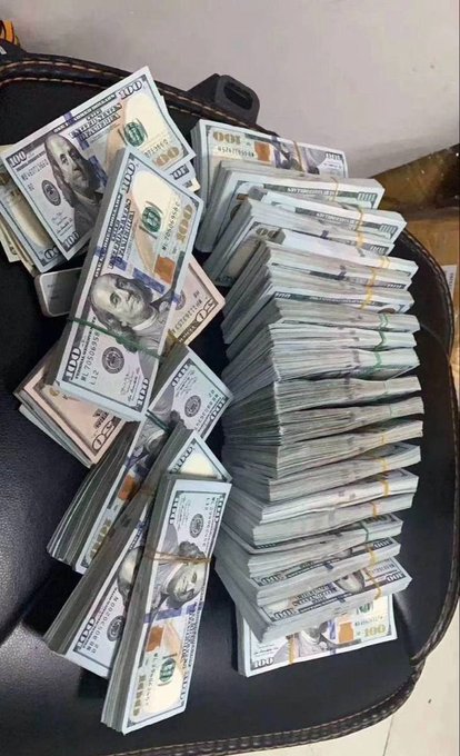 A suitcase filled with large stacks of bundled US $100 bills, appearing to contain a substantial amount of cash.