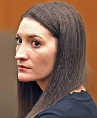 A side-profile portrait of a woman with long brown hair wearing a dark top, looking toward the camera against an orange background.