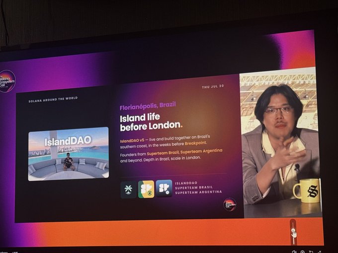 A TV screen displaying a Solana 'Breakpoint' event presentation titled 'Florianópolis, Brazil: Island life before London' about IslandDAO v5, with a man speaking on the right side of the screen.
