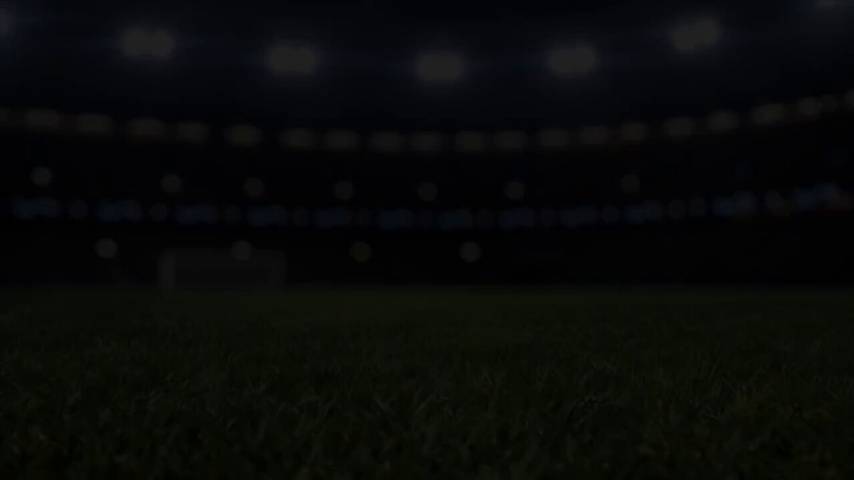 The image shows an empty soccer stadium with green grass covering most of the ground. There are no players or spectators visible on the field at this moment. The atmosphere appears dark as if it was captured during a night game, with several lights illuminating the pitch area throughout the scene. The image is related to the post because it features a screenshot of a betting app for predicting soccer match outcomes, and it is promoting an international game called Tria FC that allows users to predict the results of World Cup games, win bonus points, and participate in a $15,000 prize pool.