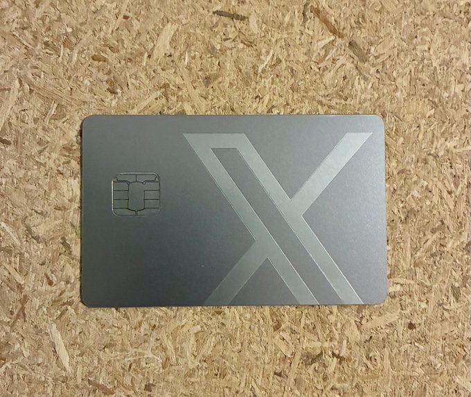 A dark grey metallic credit/debit card featuring a large embossed 'X' design and an EMV chip, photographed on a wooden surface.