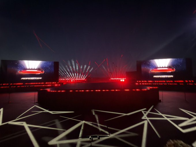 A dark stage features dramatic red laser beams shooting upward with two large screens displaying the word "MONSTER" and an illuminated logo, accompanied by the caption "The world is ready for the greatest unveil of all time," building anticipation for a major "Monster" brand event or product reveal.