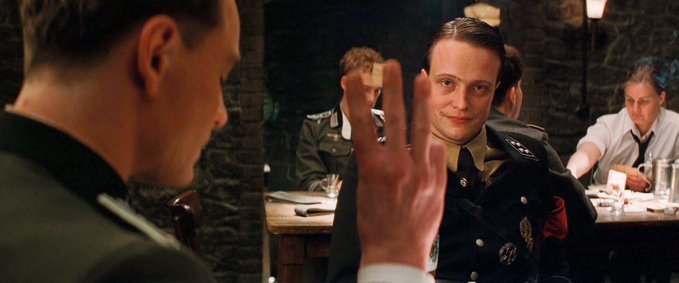 Two men in Nazi-era uniforms face each other across a table, with one holding up three fingers in a gesture reminiscent of a humorous counting scene from "Inglourious Basterds," suggesting a playful nod to the post's joke about platforms settling P&L every 15 minutes — a far more frequent interval than the dramatic "three" being counted in the film.