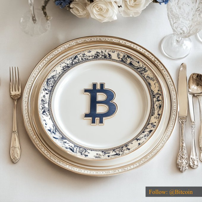 An elegant place setting features a decorative china plate prominently displaying the Bitcoin logo in its center, flanked by silver flatware and accented with white roses and crystal glassware, visually promoting Bitcoin at its $78,311.64 value.