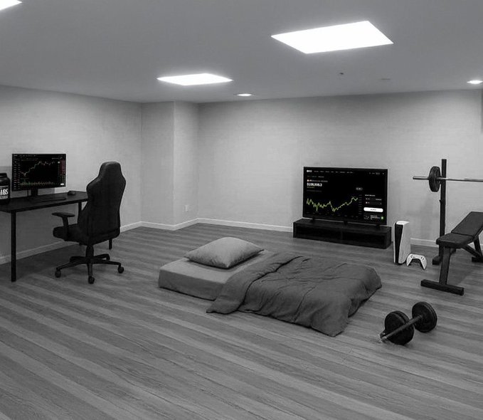 A minimalist room features a desk with a computer displaying a green chart, a mattress on the floor, a TV showing "EUR/USD" trading data, and basic gym equipment including a bench press and dumbbells — embodying the typical crypto trader's sparse, utilitarian lifestyle prioritizing screens and fitness over furnishings.