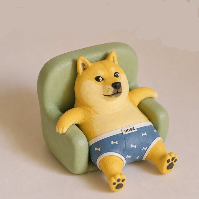 The image features a yellow toy dog figurine sitting comfortably on top of a green couch, wearing blue underwear that matches its fur color. The figurine has a pair of white paws and a tail with black spots. The background appears to be a plain white wall or surface. The caption "just another day with $DOGE" is written in the image, which seems to be a reference to the toy dog's name.
