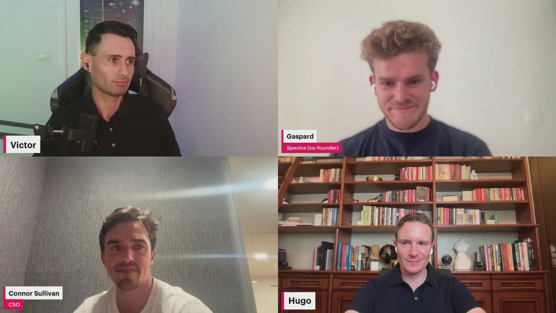 The image shows four men sitting at a table for a video call. They are all looking into the camera with smiles on their faces. The background of the image features a bookshelf filled with numerous books, suggesting that they might be discussing or sharing ideas related to literature and knowledge.