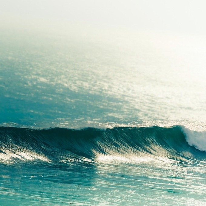 A serene photograph of ocean waves rolling in a turquoise sea under bright sunlight.