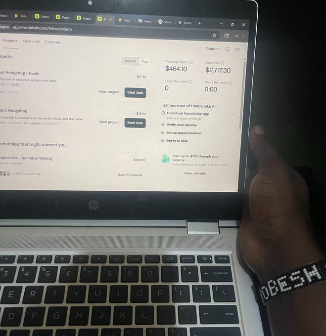 A person's hand reaches toward an HP laptop displaying the Handshake AI freelancer dashboard, showing earnings of $2,717.30 paid out and $464.10 awaiting payout across projects like "Project Hedgehog - Evals" paying $17/hr. The image visually reinforces the post's promotion of Handshake as a lucrative AI training platform, demonstrating real earnings from the platform.