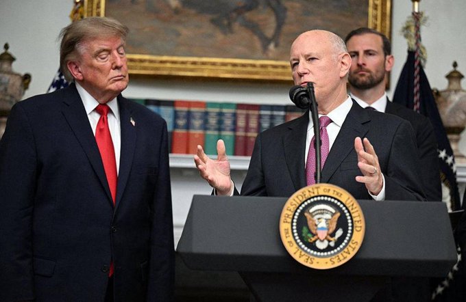 Donald Trump stands beside SEC Chair Gary Gensler, who is speaking at a podium displaying the Seal of the President of the United States.