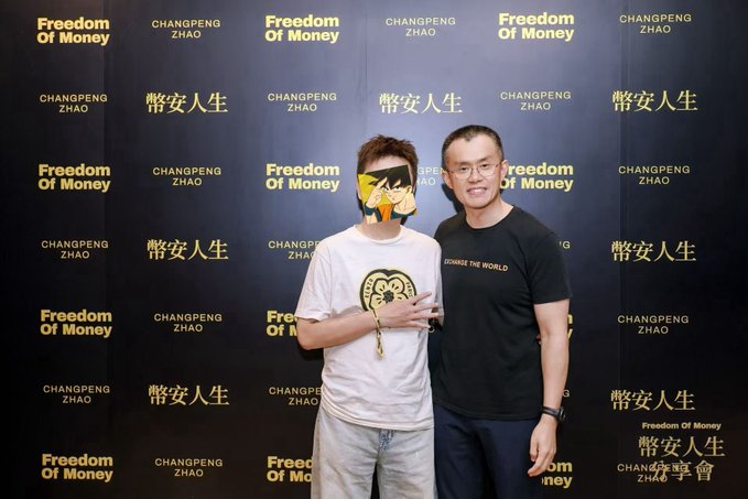 Two men pose together in front of a step-and-repeat backdrop displaying the logos 'Freedom Of Money' and 'CHANGPENG ZHAO' alongside Chinese characters '幣安人生'.