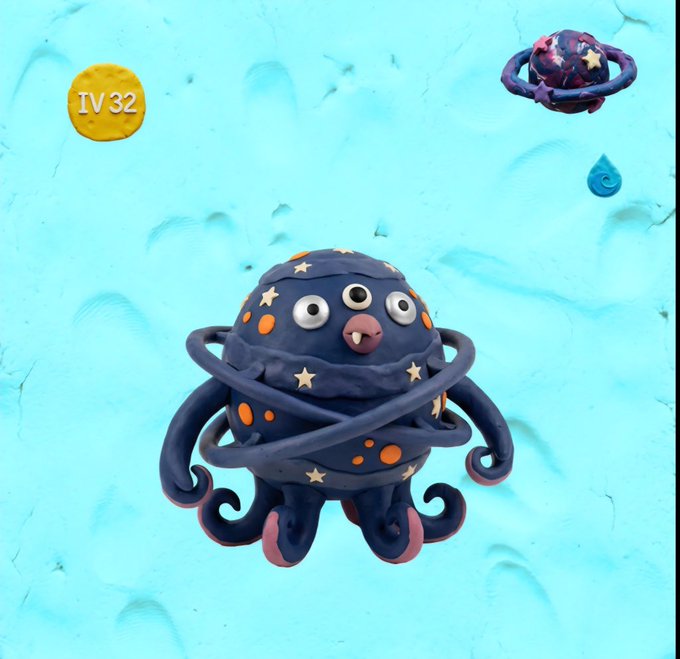 A clay sculpture of a whimsical octopus-like creature with three eyes, stars, and orange dots on its body, displayed on a light blue textured background with an 'IV32' label in the corner.