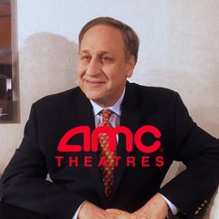 Adam Aron, CEO of AMC Theatres, is pictured in a suit with the red AMC Theatres logo prominently displayed across the image, visually connecting to the news of him demanding Robinhood cease and desist listing tokenized AMC stock.