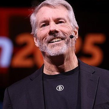 Photo of Michael Saylor, the MicroStrategy executive known for his Bitcoin advocacy, wearing a black blazer with a Bitcoin logo pin and speaking on stage.