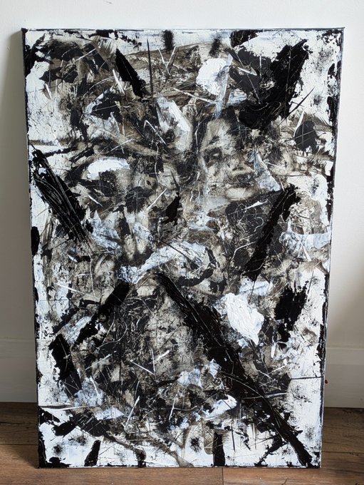 An abstract mixed-media painting on canvas featuring black, white, and earthy tones with chaotic scratched lines and textured layers, leaning against a white wall on a wooden floor.