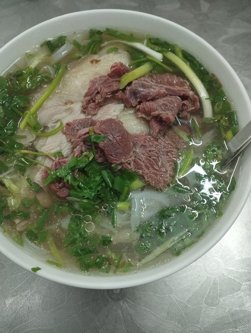 A bowl of Vietnamese pho soup containing noodles, beef slices, and green herbs in a clear broth.