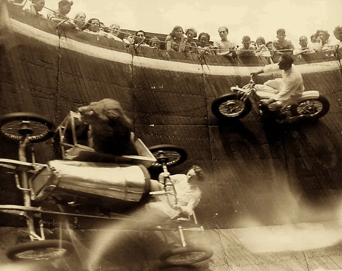 A black-and-white vintage photograph shows motorcyclists performing death-defying stunts on a "Wall of Death" carnival ride, with one rider on a motorcycle defying gravity along the vertical wooden wall while spectators watch from the top, and another rider appearing to crash in the foreground amid a cloud of smoke. The image does not contain any visible text, numbers, or names matching those mentioned in the accompanying post about Linn's Leverage and DeFi protocols, suggesting the photo serves as a dramatic visual metaphor for high-risk financial maneuvers rather than a direct depiction of the crypto-related content.