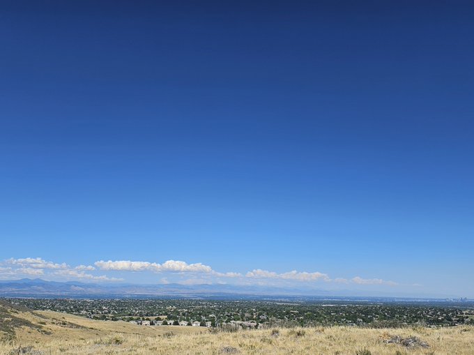 A scenic landscape view showing a vast blue sky above a wide valley with distant mountains and clouds on the horizon.