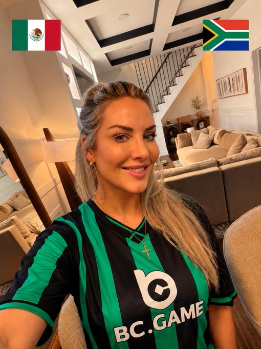 The image features a woman wearing a green and black striped soccer jersey, posing for a photo with her arms around herself. The caption of the image reads "Game day is finally here! Mexico or South Africa ... who’s getting the first win? I’ve got my eyes on the match... and the BC rewards Drop your prediction below!".