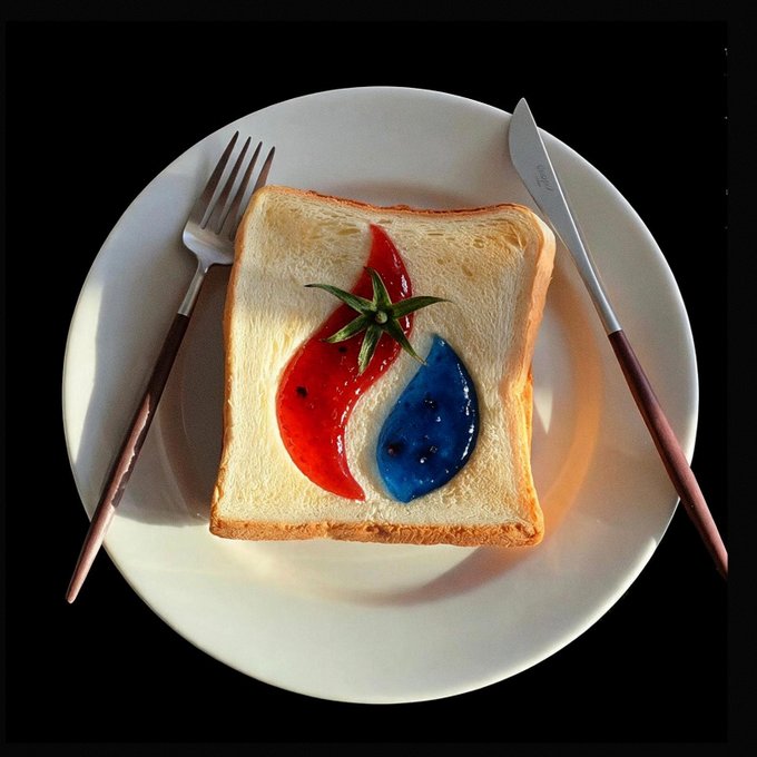 A slice of white bread on a white plate is artistically decorated with red and blue jelly forming a yin-yang shape, garnished with a sprig of rosemary, flanked by a fork and knife.