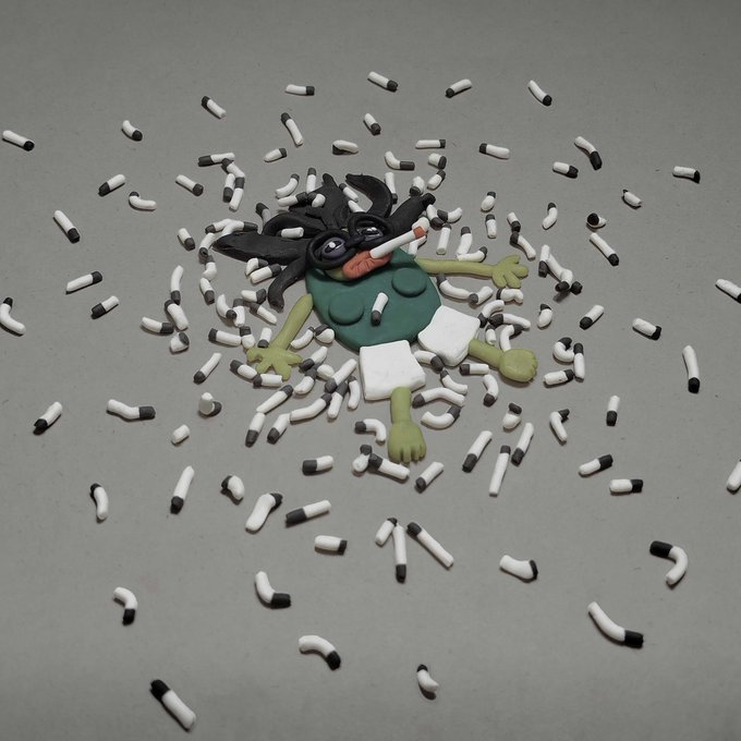 A claymation-style figure with wild black hair lies on a gray surface surrounded by scattered black and white pill capsules.