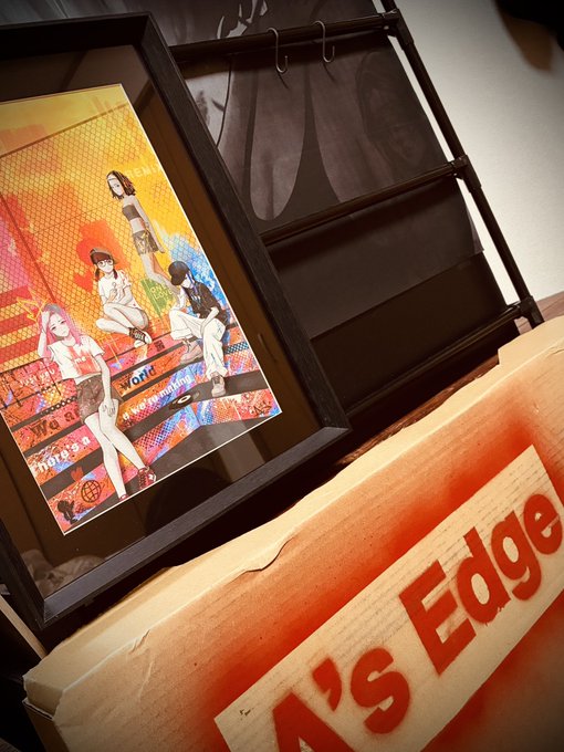 A framed pop-art style illustration of figures on a street rests next to a wooden rack and a worn bumper sticker partially reading "A'S Edge".